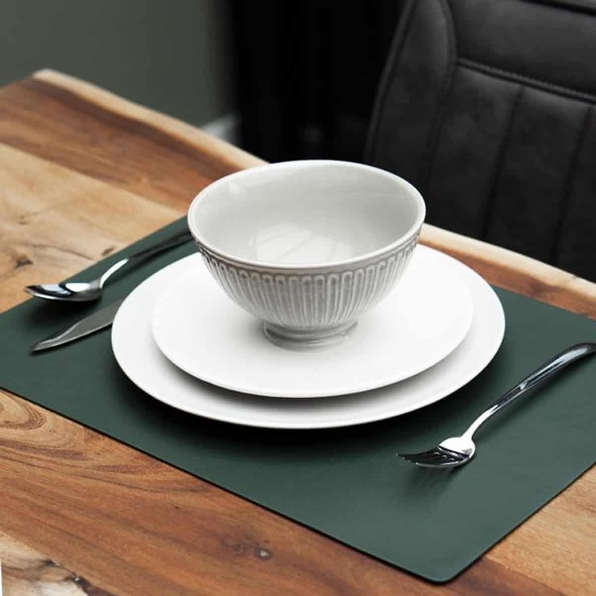 Groene lederlook placemat met wit servies op een houten tafel